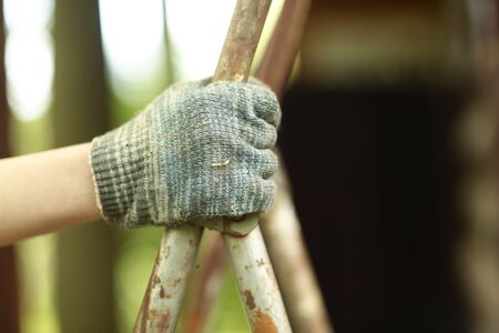 close up photo of human hand in glove holding ladder on country house backgroundの写真素材