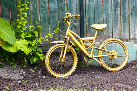 golden bicycle as a formal garden decoration on wooden blue fence background の写真素材