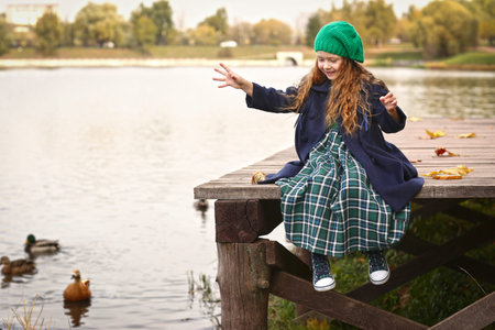 Irish little red haired girl outdoor photo on fall lake landscape background feeding ducksの写真素材