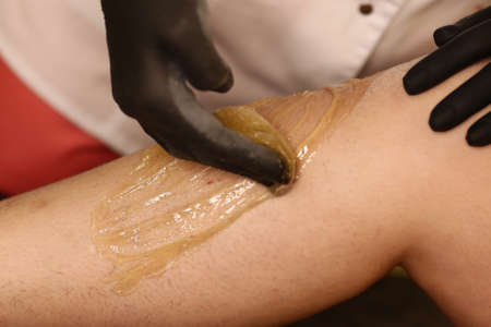 cosmetician hands make depilation procedure on woman legs with waxの写真素材