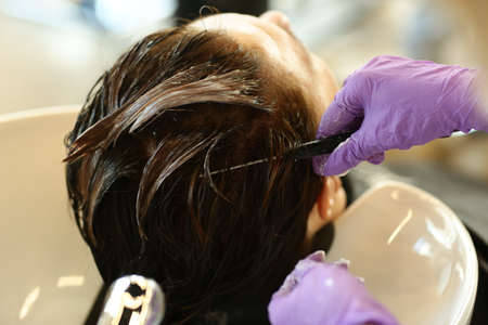 hairdresser hand with hair dye making haircut and hair coloring on client closeup photoの写真素材