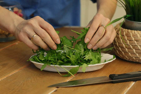 arugula salad in plate with human hands and knife closeup photo on kitchen tableの写真素材