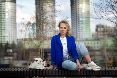 blond woman in blue jacket, jeans and white blouse closeup photo on urban landscape backgroundの写真素材