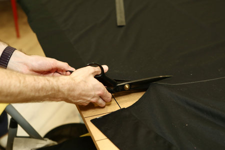 tailor hands with scissors cut black fabric closeup photo in sewing school