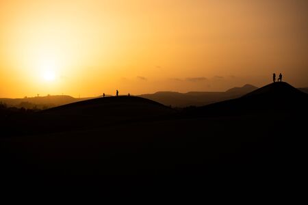 Desert sand dunes during sunset with silhouettes in the background of people taking photographsの写真素材