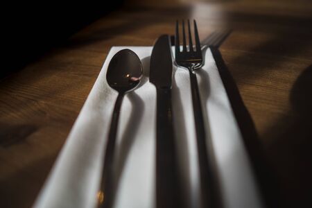 Some silverware, cutlery sat on a white napkin on a wooden table in a cafe settingの写真素材