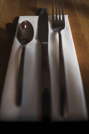 Some silverware, cutlery sat on a white napkin on a wooden table in a cafe settingの写真素材