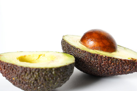 An avocado sliced in half to reveal the core against a plain whit background