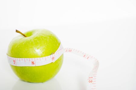 A granny smith green apple with a measuring tape wrapped around it against a plain white backgroundの写真素材