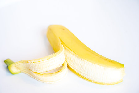 A Whole banana with the skin peeled back against a plain white backgroundの写真素材