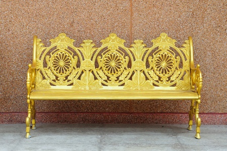 golden iron bench on brown cement wallの写真素材