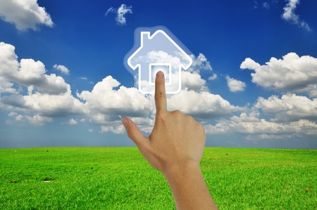 Hand pressing home symbol  on  grassland and blue skyの写真素材