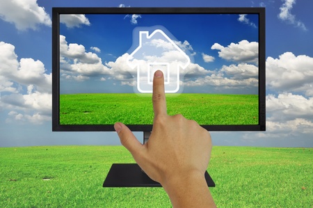 Hand pressing home symbol  on  grassland and blue sky  in computor LCD monitorの写真素材