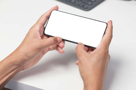 Two hand holding smartphone with blank screen, with office desk environmentの写真素材
