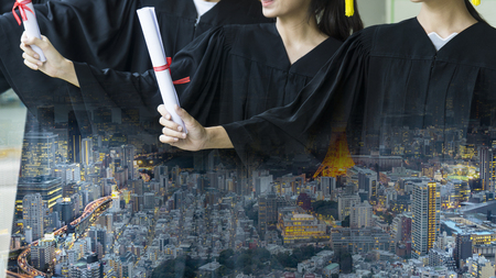 the people with black graduation gowns hold the diploma stand. With Overlay nighttime modern cityの写真素材