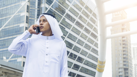 Arab man stands and uses mobile phone at outdoor city space at morning dayの写真素材