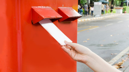Hand with postcard and drop in red mail postbox