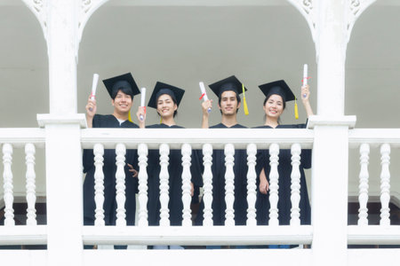 students in feeling happy with graduation gowns stand at corridor building.の写真素材