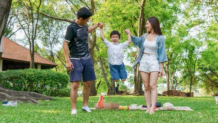 Cute boy jump and hold the hand mother and father in park.Happy family picnic concept.の写真素材