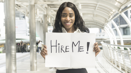 Portrait business african woman holds paper board with word hire me at pedestrian outdoor cityの写真素材