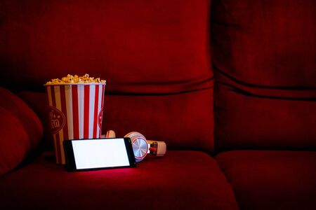 mobile phone with empty white bright screen with popcorn bucket on the red sofa. Concept of streaming TV on internet phone.の写真素材