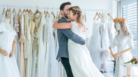 Portrait of Couple love or groom and bride hug and try to fitting suit or dress in wedding fashion dress up interior studio with hug or kiss as romantic concept.の写真素材