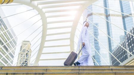 arab man carry a suitcase at business city walk in the business landmark city with the modern steel structure and exterior wall modern buildingの写真素材