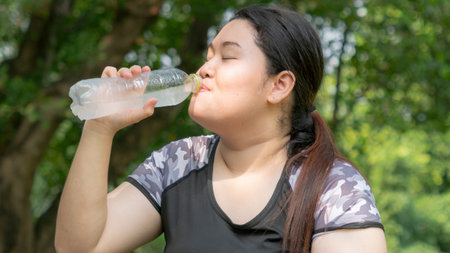 sport woman. Asian sport fat girl drink water from plastic bottle on the hand in summer hot day at...
