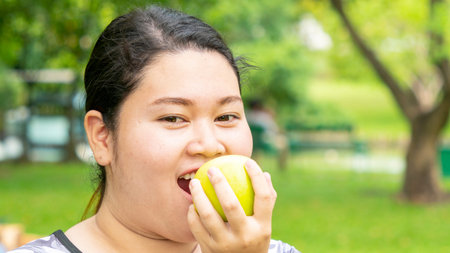 sport woman. Young curvy fat woman in sport clothes on holding a green apple in her hand and eating...