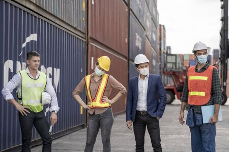 group people worker is wearing protection mask face and safety helmet and wearing suit safety dress With background of container cargo warehouse. Concept of industry worker operating.の写真素材