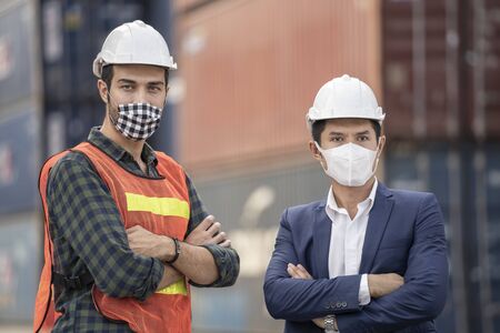 Business man and  Factory workers wearing in a medical mask and safety cloth at outdoor factory cargo warehouse.の写真素材