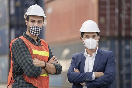 Business man and  Factory workers wearing in a medical mask and safety cloth at outdoor factory cargo warehouse.の写真素材