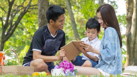 mother and father are teaching kid in park with book.Happy family picnic concept.の写真素材