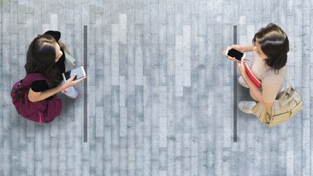 Human life in Social distance. Aerial top view with two student women with smartphone stand at grey pavement street road with empty space.の写真素材