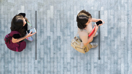 Human life in Social distance. Aerial top view with two student women with smartphone stand at grey...