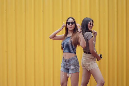 Young asian joyful couple women in summer fashion suite standing in yellow steel plate background....