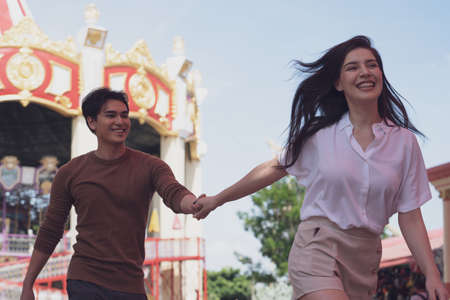 A couple in love of young funny and happy woman and man walking or running at amusement park background. Human emotions, youth, love and lifestyle concept.の写真素材