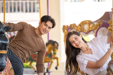 Young joyful couple man and woman riding on horse at Carousel amusement park. Concept happy and lovely life of teenager.の写真素材