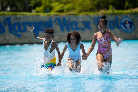 African kid girls and boy running to swimming water pool at amusement park.  Concept kid are expressing pure joy and excitementの写真素材