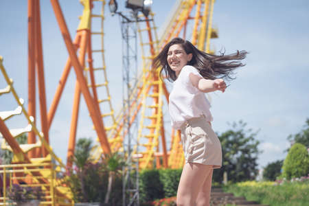 tourist young woman standing in feeling happy at front of 
Roller coaster in amusement park. Concept happy life in the vacation in summer day.の写真素材
