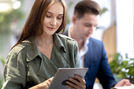 Portrait of happy woman holding tablet device and sitting at coffee cafe counter bar with people colleague at background. Concept business coffee time with smart technology working.の写真素材
