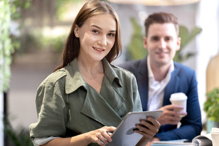 Portrait of happy woman holding tablet device and sitting at coffee cafe counter bar with people colleague at background. Concept business coffee time with smart technology working.の写真素材