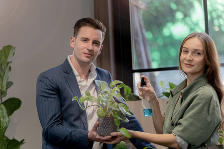 Portrait of happy businessman and woman check and treat green trees plant leaves at indoor building garden. Concept office space with biophilia nature.の写真素材