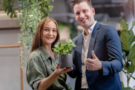 Portrait of happy businessman and woman hold and treat plat pot green trees plant leaves at indoor building garden. Concept office space with biophilia nature.の写真素材