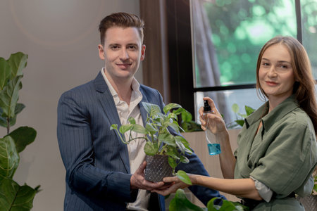 Portrait of happy businessman and woman check and treat green trees plant leaves at indoor building garden. Concept office space with biophilia nature.の写真素材