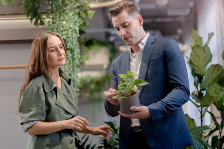 Portrait of happy businessman and woman hold and treat plat pot green trees plant leaves at indoor building garden. Concept office space with biophilia nature.の写真素材