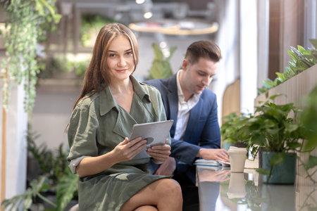 Portrait of happy woman holding tablet device and sitting at coffee cafe counter bar with people colleague at background. Concept business coffee time with smart technology working.の写真素材