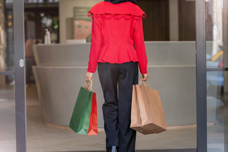 woman in red dress holding shopping bag and walking to shop building. Concept people activity in shopping festival season christmas and new year.の写真素材