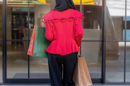 woman in red dress holding shopping bag and walking to shop building. Concept people activity in shopping festival season christmas and new year.の写真素材