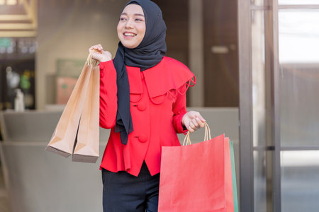 happy face muslim woman in red dress holding shopping bag and walking out shop building. Concept people activity in shopping festival season christmas and new year.の写真素材